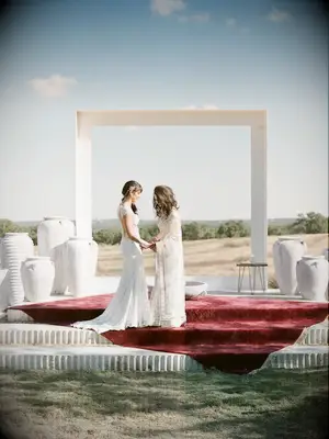 two brides standing in front of oversized white square frame overlooking hillside venue