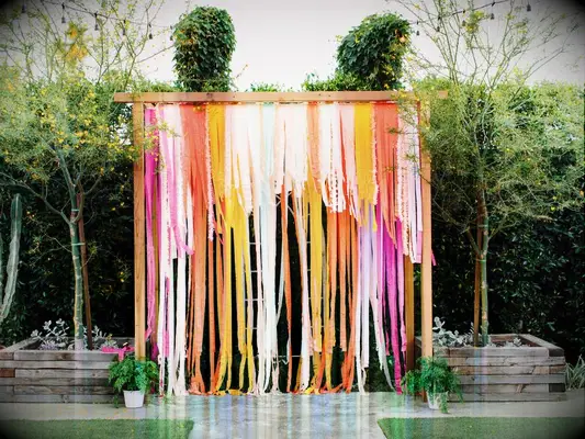 colorful wedding arch alternative made from paper streamers in pink, orange yellow and blue