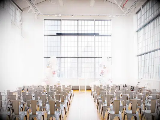 indoor wedding ceremony decorated with white and clear balloon pillars at altar