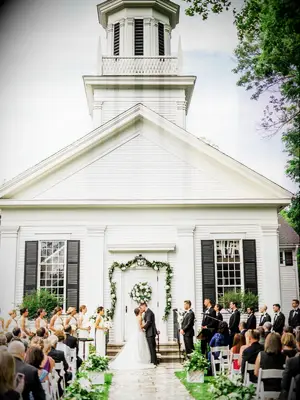 bride and groom kiss in front of white wedding chapel door decorated with greenery garland