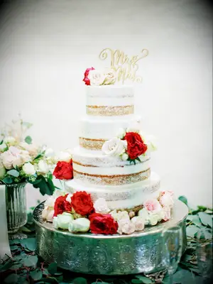 four tier semi naked wedding cake decorated with white, red and blush roses with gold mr. & mrs. cake topper