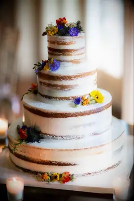 four tier semi naked wedding cake decorated with blue, yellow, orange and purple wildflowers