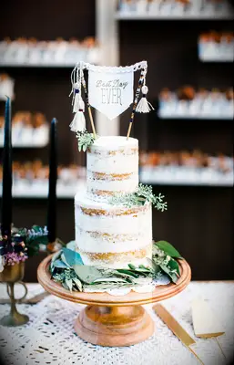 two tier semi naked wedding cake with eucalyptus and fringe pennant banner cake topper