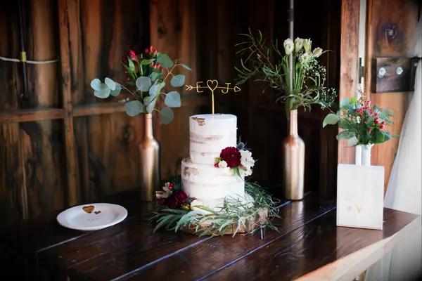 fall semi naked wedding cake decorated with burgundy dahlias, eucalyptus and gold initial cake topper