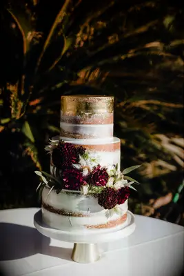 modern semi naked wedding cake with edible gold leaf on the top tier and burgundy dahlias cascading down the front of the cake