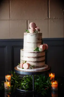 two tier semi naked wedding cake decorated with pink macarons and greenery sprigs