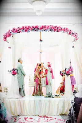 Couple underneath pink-and-white mandap in ballroom