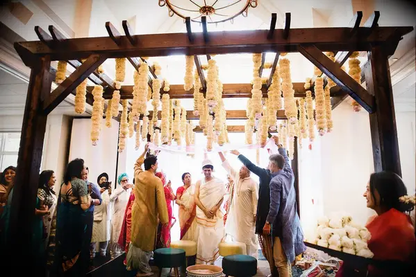 Wedding ceremony taking place beneath wood mandap with orange flower accents