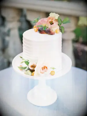 One-tier cake on white cake stand with fresh fruit and flower decorations