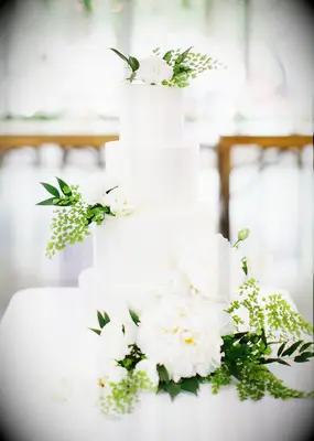 All-white four-tier cake with white flowers and greenery decorations.