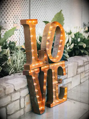 large gold vintage marquee letters spelling LOVE propped up against a stone wall 