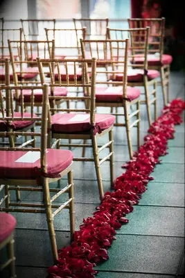 indoor wedding ceremony aisle lined with red rose petals along rows of gold chiavari chairs with red seat cushions