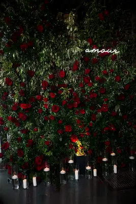 greenery wall decorated with red roses and amour written in white neon letters 