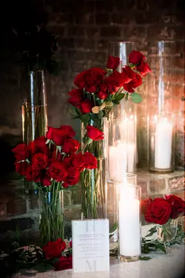 red long-stem roses in glass cylinder vases with white pillar candles 