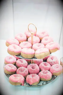 pink frosted donuts with white sprinkles displayed on two-tier cookie stand at valentine