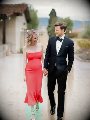 bride wearing strapless red fitted midi dress holds hands with groom in black tuxedo walking at santa barbara historical museum