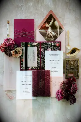 wedding invitation flatlay with blush envelopes, burgundy and black floral print invitations and gold accents