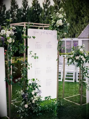 Seating chart suspended from gold structure and covered in greenery