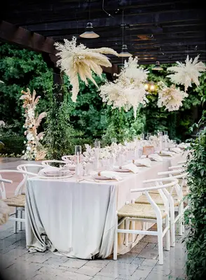 outdoor wedding reception with clusters of white pampas grass hanging above long banquet table