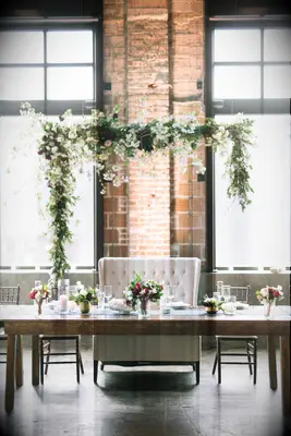 wedding sweetheart table with greenery garland and flower installation hanging against the wall behind loveseat