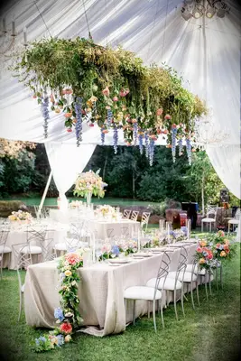 long wedding reception table with garden-inspired hanging centerpiece of blue delphinium, greenery, pink dahlias and yellow roses