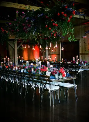 indoor wedding reception with hanging jewel tone purple blue and red flower centerpiece accented with edison bulbs on long cords 