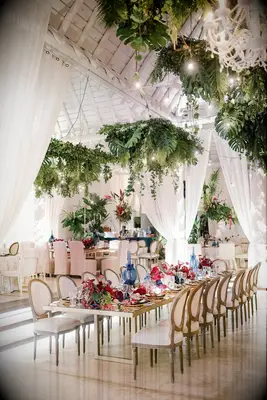 indoor wedding reception with tropical monstera leaves hanging above long wooden banquet table