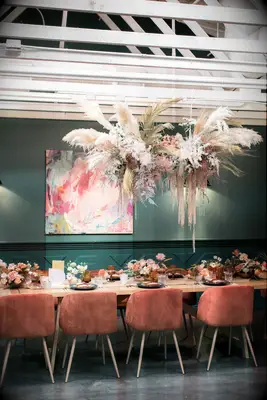restaurant wedding venue with hanging pampas grass installation above long banquet table with orange velvet chairs