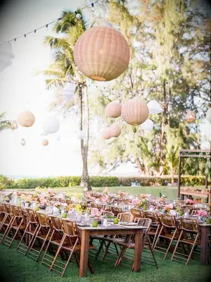 Tropical wedding reception with farm tables and woven lanterns