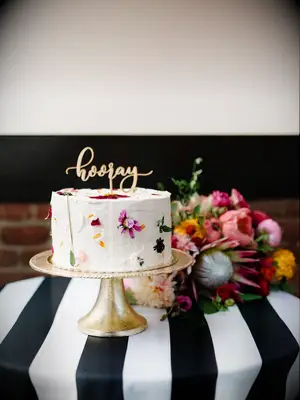 one-tier simple wedding cake decorated with edible flower petals and gold hooray cake topper on gold cake stand