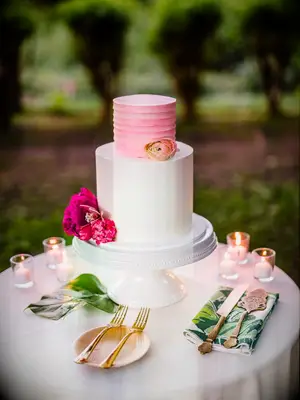 simple two tier wedding cake with smooth white buttercream and pink peony on the bottom tier and light pink textured buttercream on the top tier