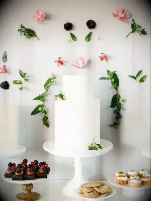 white simple two tier wedding cake against a backdrop of light pink orchids and greenery