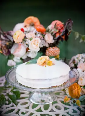 simple one-tier wedding cake with white buttercream frosting and yellow ranunculus on glass cake stand