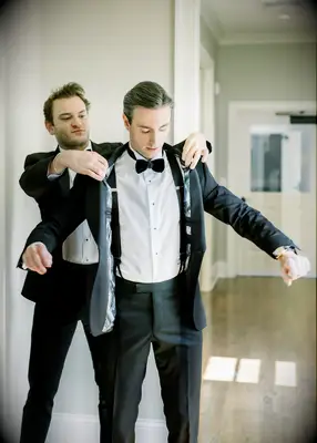 Groom is Helped into His Classic Black Tuxedo Jacket With Foliage-Print Liner