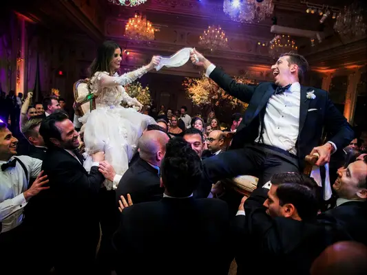 Bride and groom lifted in chairs by groomsmen during traditional Hora