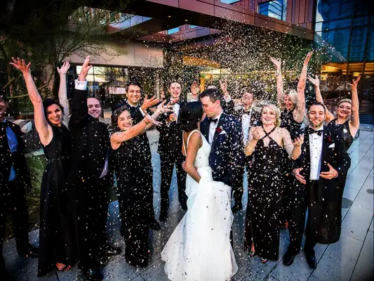 Bride and groom kissing under confetti toss thrown by wedding party