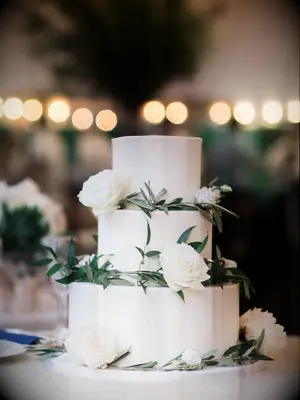 three tier white wedding cake decorated with greenery and white roses
