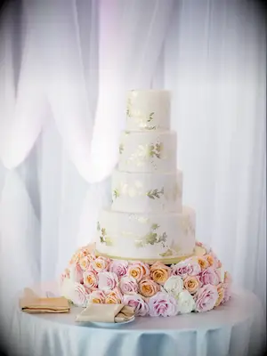 glam four tier wedding cake with gold metallic leaf design atop a bed of blush and orange roses