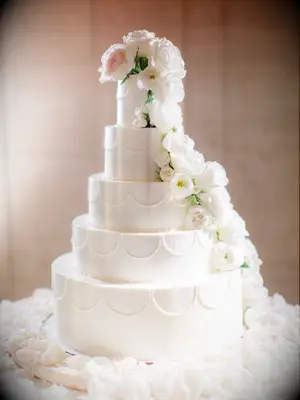 four tier elegant flower wedding cake with hand piped scallop pattern and ivory roses cascading down the side