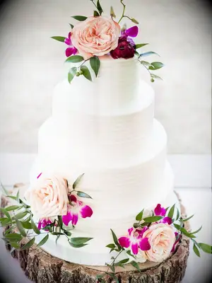 four tier buttercream wedding cake with pink roses, fuchsia orchids and greenery displayed on wooden tree cake stand