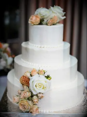 four tier white wedding cake with beige and ivory roses and hand-piped trimming