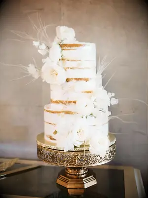 three tier naked wedding cake with white flowers and white ostrich feathers