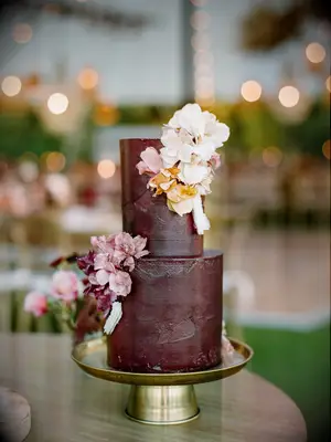 two tier brown wedding cake with blush, white and pale orange flowers on gold cake stand