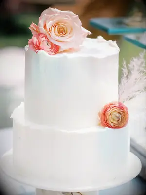 small white wedding cake with ruffled edges, peach rose, orange ranunculus and pampas grass