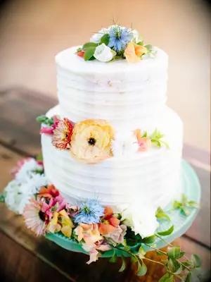 two tier buttercream wedding cake with blue yellow orange and pink wildflowers