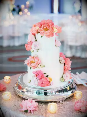 three tier white wedding cake on silver round base with lilac roses and coral peonies