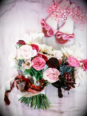 Beside a pair of pink velvet shoes, a stunning bouquet of pinks and wine reds sits.