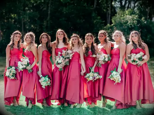 Bridesmaids stand together with their bouquets in the sun, each wearing a hot print gown.