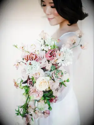 A bride holds a cascading bouquet of flowers in different shades of pink.
