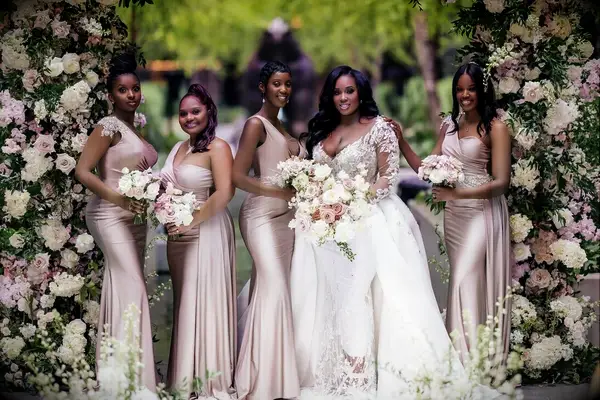 A bride and her bridesmaids pose for a photo, the wedding party wearing dusty rose gowns.